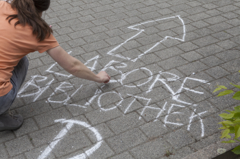 Eine Frau schreibt mit Kreide auf den Boden, dort stehen die Worte Labore und Bibliothek unter einem Pfeil