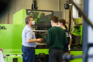 drei Personen vor einer Maschine in der Maschinenhalle