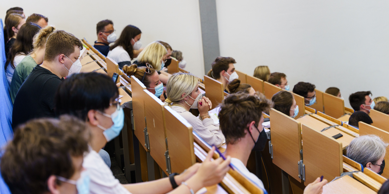 In den Sitzreihen eines Hörsaals sitzen viele Menschen