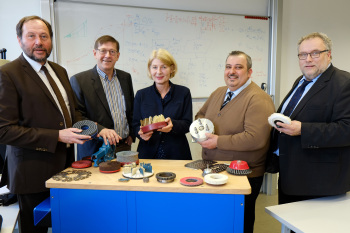 Fünf Personen, vier Männer und eine Frau, stehen hinter einem Tisch mit Materialien aus der Gründung.