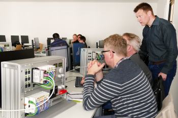 Drei Männer sitzten vor Bildschirmen in einem Seminarraum