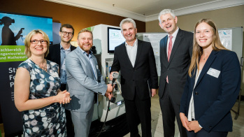 Zwei Frauen und vier Männer stehen neben einer Tanksäule für Elektroautos