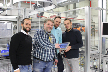 Vier Männer stehen vor Maschinen, ein Mann hält ein Tablet in der Hand