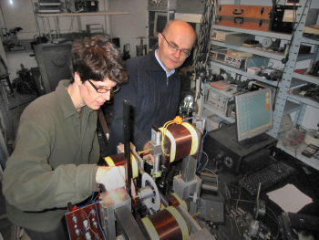 Eine Frau spannt ein Stoffstück in eine Maschine mit Spulen ein, ein Mann beobachtet sie dabei