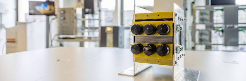 Ein gelber Block mit sechs schwarzen Knöpfen steh auf einem Tisch.