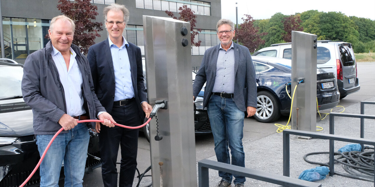 Hans Jürgen Rost, Dr. Peter Westerbarkey und Dr. Michael Hübert stehen an der Ladesäule der FH Bielefeld