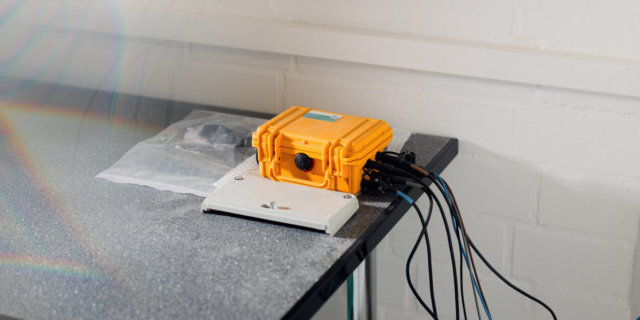 Foto: Ein gelber kleiner Kasten liegt auf einem Tisch an der Seite sind Kabel angeschlossen