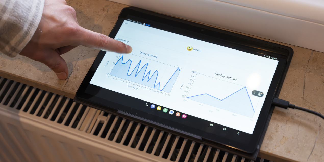 Foto: Finger der auf ein Tablet zeigt wo tägliche Aktivitäten aus dem KognieHome angezeigt werden und wie der Status auf Happy steht