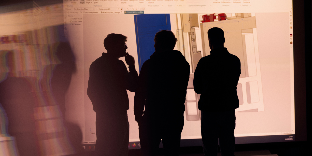 Die Wissenschaftlichen Mitarbeiter des Teams von Professor Ziebart stehen in einem abgedunkelten Raum mit dem Rücken zur Kamera Ihre Schattenumrisse sind in Richtung einer großen Videowand gedreht auf der der Grundriss eines Raumes zu sehen ist.