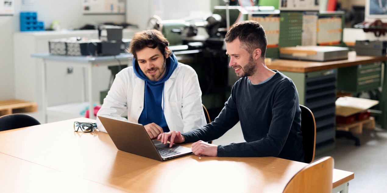 Patrick Obermark und Christian Bill sitzen vor einem Laptop an einem Tisch