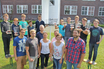Die Schüler stehen auf Bierbänken neben dem weißen Sovonius-Kraftwerk und halten ihre Modelle in der Hand. Die betreuer stehen vor den Bänken.