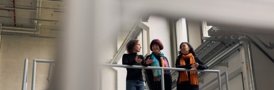 Drei Personen stehen auf einer Plattform in der Experimentierhalle der HSBI