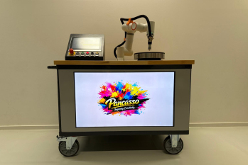 Foto: Der Pancake-Roboter PanCasso von vorne mit Logo auf dem Bildschirm und dem Roboterarm über dem Pfannkuchen-Eisen