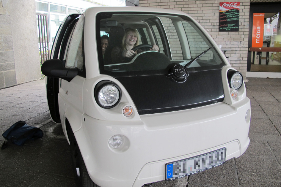 Eine Schülerin sitzt am Steuer eines kleinen schwarz-weißen Elektroautos.