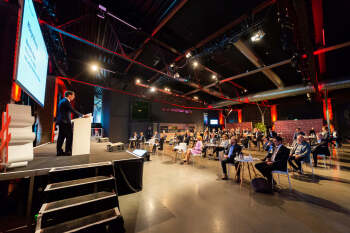 2020-09-09 VM-Ein mann steht auf einer Bühne, vor ihm sitzen an mehreren Tischen Menschen.NRW_Buendnistag-Bielefeld-0823_Seite