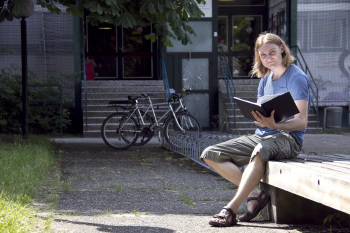 Masterstudent Jono Kulecki ließt in seiner Masterabreit während er auf einer Bank vor dem Fachbereich Sozialwesen sitzt.