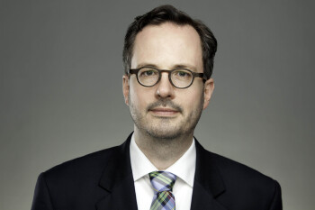Ein Mann mit Brille und im schwarzen Anzug schaut in die Kamera.
