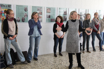 Prof. Muth steht vor einigen Gästen. Hinter ihnen an der Wand hängen die Plakate der Austellung.
