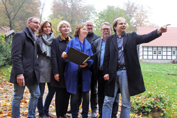 Die Gruppe steht im Garten, guckt in die Pläne und auf das Gelände, wo der Garten entstehen soll.