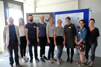 Eine Gruppe von Personen steht nebeneinander vor Pinnwänden, die Personen blicken in die Kamera.