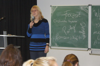 Prof. Dr. Gudrun  Dobslaw steht mit einem Mikro in der hand vor einer Tafel und redet zu Studierenden.