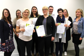 Acht Frauen und ein Mann schauen in die Kamera, einige halten eine Urkunde in den Händen.