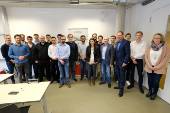 Gruppenfoto von stehenden Personen in einem Raum.