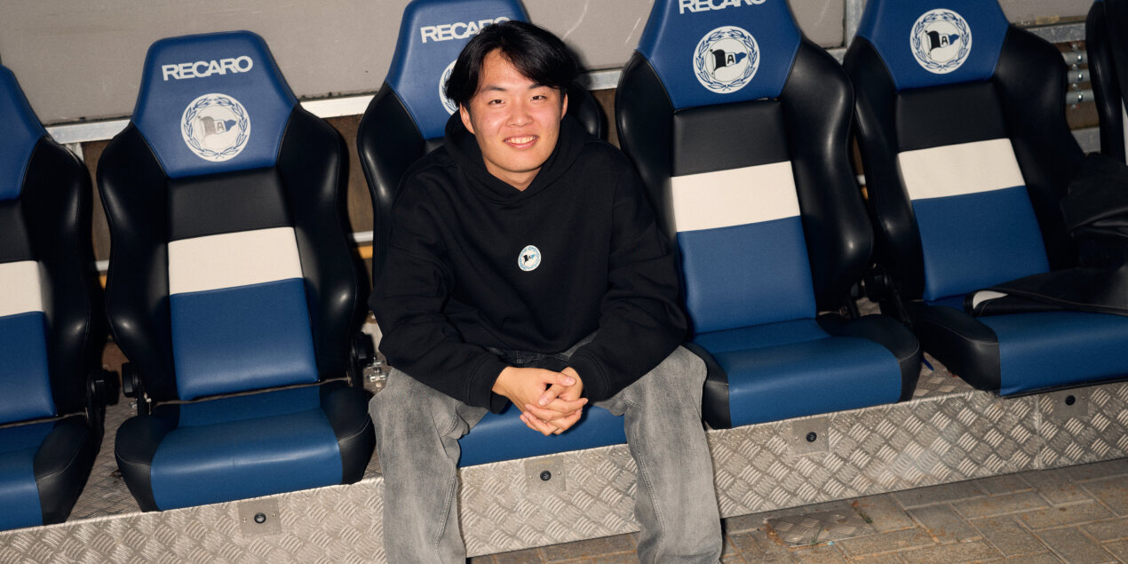 The student is sitting on the players' benches in the soccer stadium.