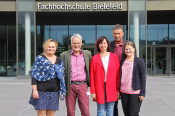 Drei Damen und zwei Herren stehen vor dem Haupteingang der FH Bielefeld.