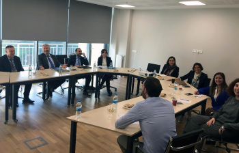 9 Personen sitzen an Tischen in U-Form.