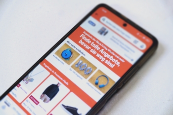 Auf einem Tisch liegt ein Handy, auf dem Bildschirm eine Oberfläche mit Angeboten und Werbung