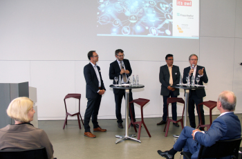 Vier Herren stehen vor einer Präsentation vor Zuschauerinnen und Zuschauern.