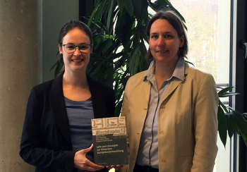 Zwei Frauen, stehend, halten ein Buch in der Hand.