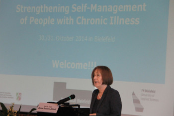 Beate Rennen-Allhoff steht hinter einen Rednerpult und vor einer Powerpoinpräsentation mit dem Titel des Symposiums.