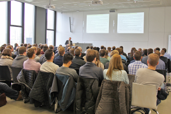 Prof. Wiemann steht vor den 110 Teilnehmern, die in mehreren Stuhlreihen hintereinander sitzen.