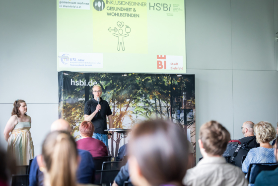 Dirk Bruland steht im Konferenzbereich der HSBI vor Publikum und spricht in ein Handmikrofon