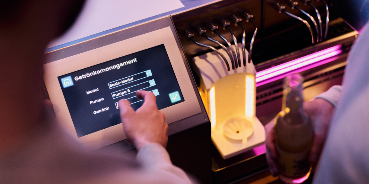 eine Person wählt etwas am Bedienfeld des Cocktailaitomaten aus