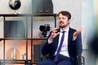 Ein Mann sitzt auf einem Stuhl und gestikuliert beim Sprechen mit den Händen.