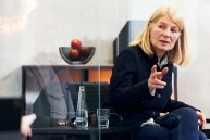 Eine Frau sitzt auf einem Stuhl, sie beugt sich nach vorne und gestikuliert.