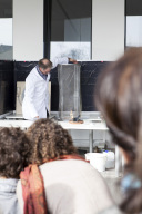 Ein Mann mit Kittel steht vor einer Säule in der etwas brennt