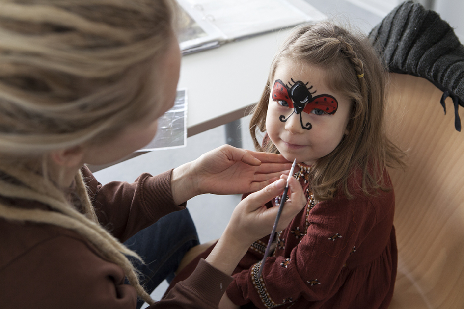Ein Junge und ein Mädchen lassen sich von zwei Frauen schminken