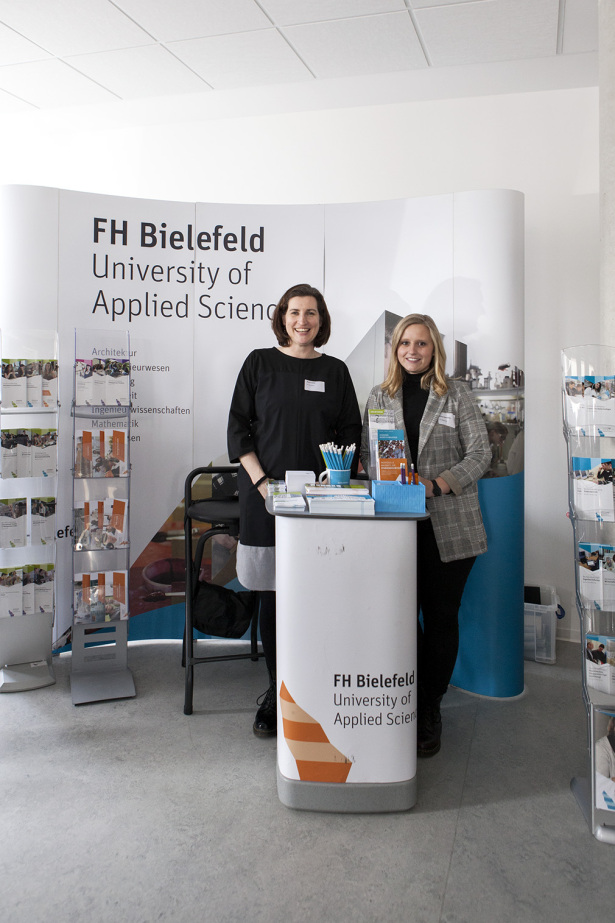 Zwei Frauen stehen vor einem Aufsteller mit dem Schriftzug der FH Bielefeld