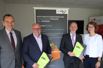 Drei Männer und eien Frau stehen vor einem Aufsteller