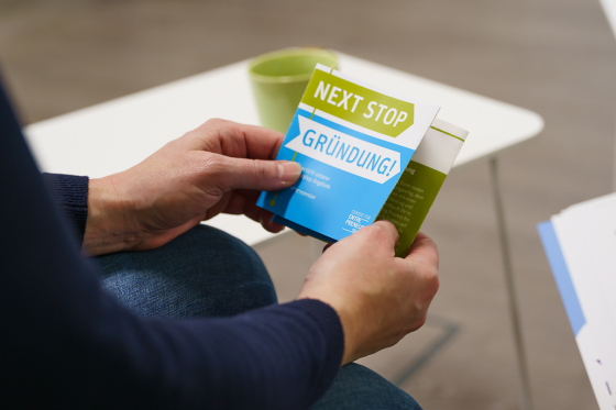Foto: Eine Person hält einen Flyer mit der Aufschrift Next Step Gründung in der Hand
