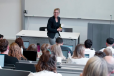Foto: Susanne Nienaber steht in einem Hörsaal vor einem Seminar in der hand hält sie ein Buch