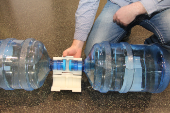 Eine Person hält ein Kunststoffteil an den Öffnungen von zwei Wasserkanistern fest