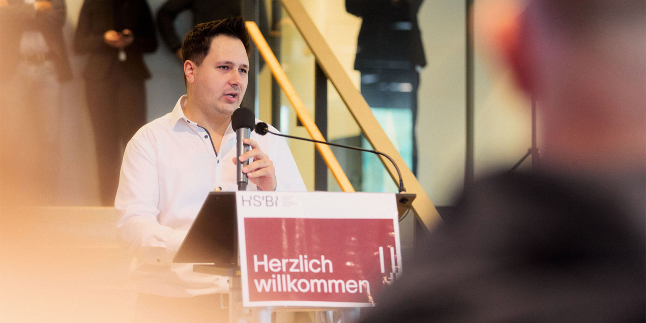 Foto: Marco Kolarevic steht am Rednerpult und spricht zu den Studierenden