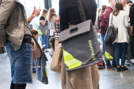 Eine Studentin hat die Tasche über der Schulter, im Hintergrund sieht man weitere Personen mit Taschen.