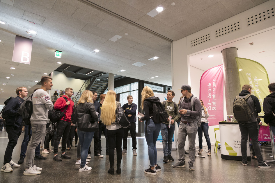 Eine Gruppe von 15 Personen stehen vor einem Stand und warten