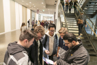 Fünf Studenten stehen in einer Runde und schauen auf einen Flyer in ihren Händen